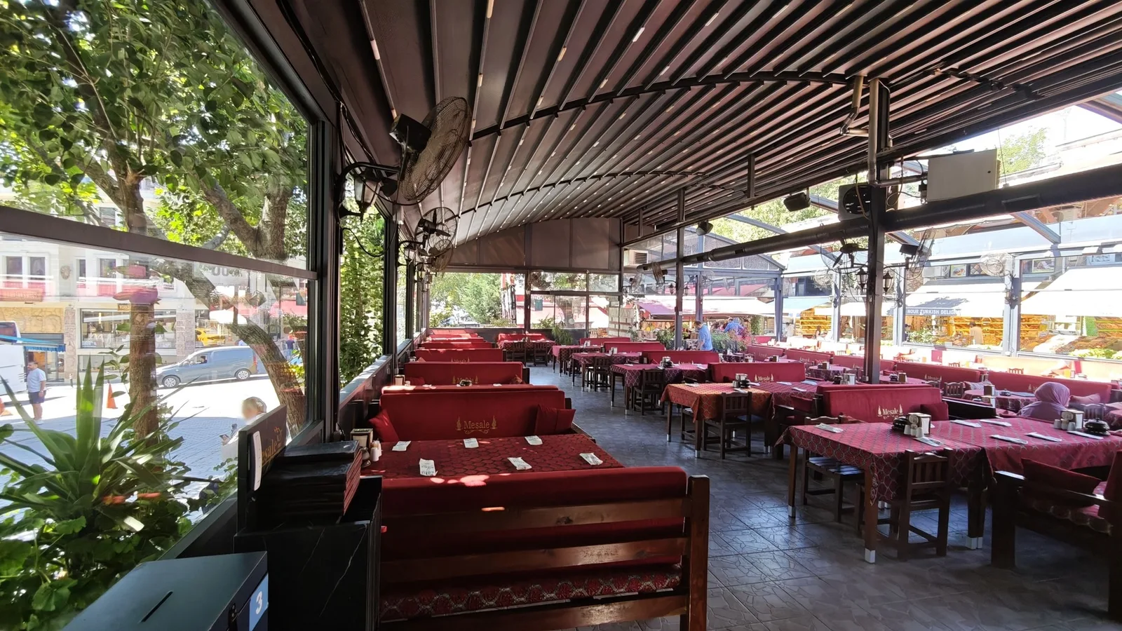 Cam kenarındaki masalar ve bahçeyi çevreleyen yeşillik
